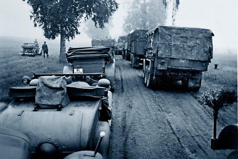 Deutsche Soldaten fahren in Autos und Militärlastern eine Feldstraße entlang