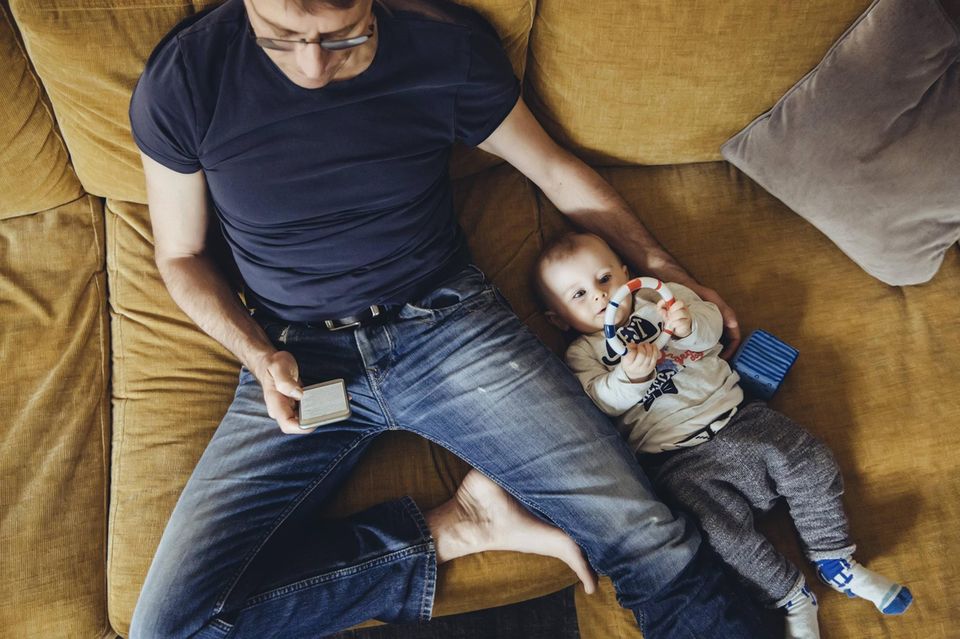 Ein Vater schaut auf das Hand und beachtet sein Baby nicht