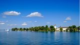 Das weiße Kloster mit Zwiebelturm zwischen den Bäumen auf einer Insel in einem sehr blauen See.