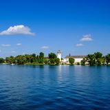 Das weiße Kloster mit Zwiebelturm zwischen den Bäumen auf einer Insel in einem sehr blauen See.