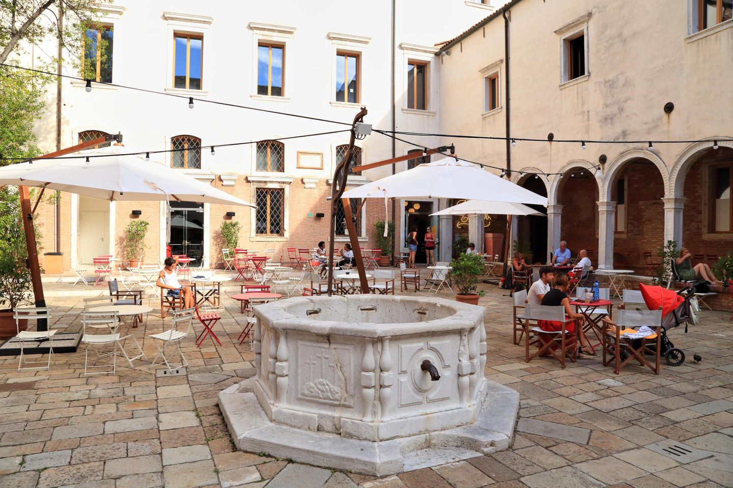 Alter Brunnen, Sonnenschirme und Tische im Innenhof des ehemaligen Klosters.