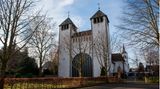 Kirche mit zwei Türmen und großer Portaltür zwischen Bäumen. Der Himmel ist blau.
