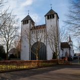 Kirche mit zwei Türmen und großer Portaltür zwischen Bäumen. Der Himmel ist blau.