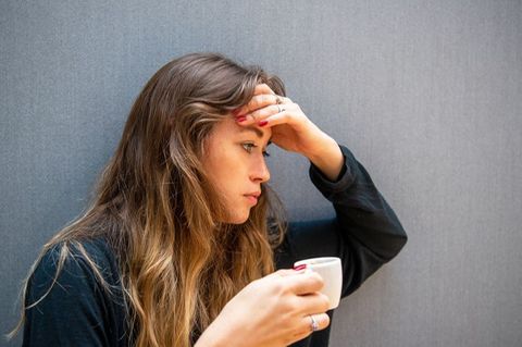 Eine Frau hält sich den Kopf und einen Kaffee