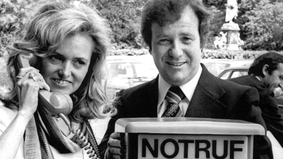 Ute Steiger posiert neben ihrem Mann Siegfried 1976 vor einer Notrufsäule, deren Hörer sie in der Hand hält