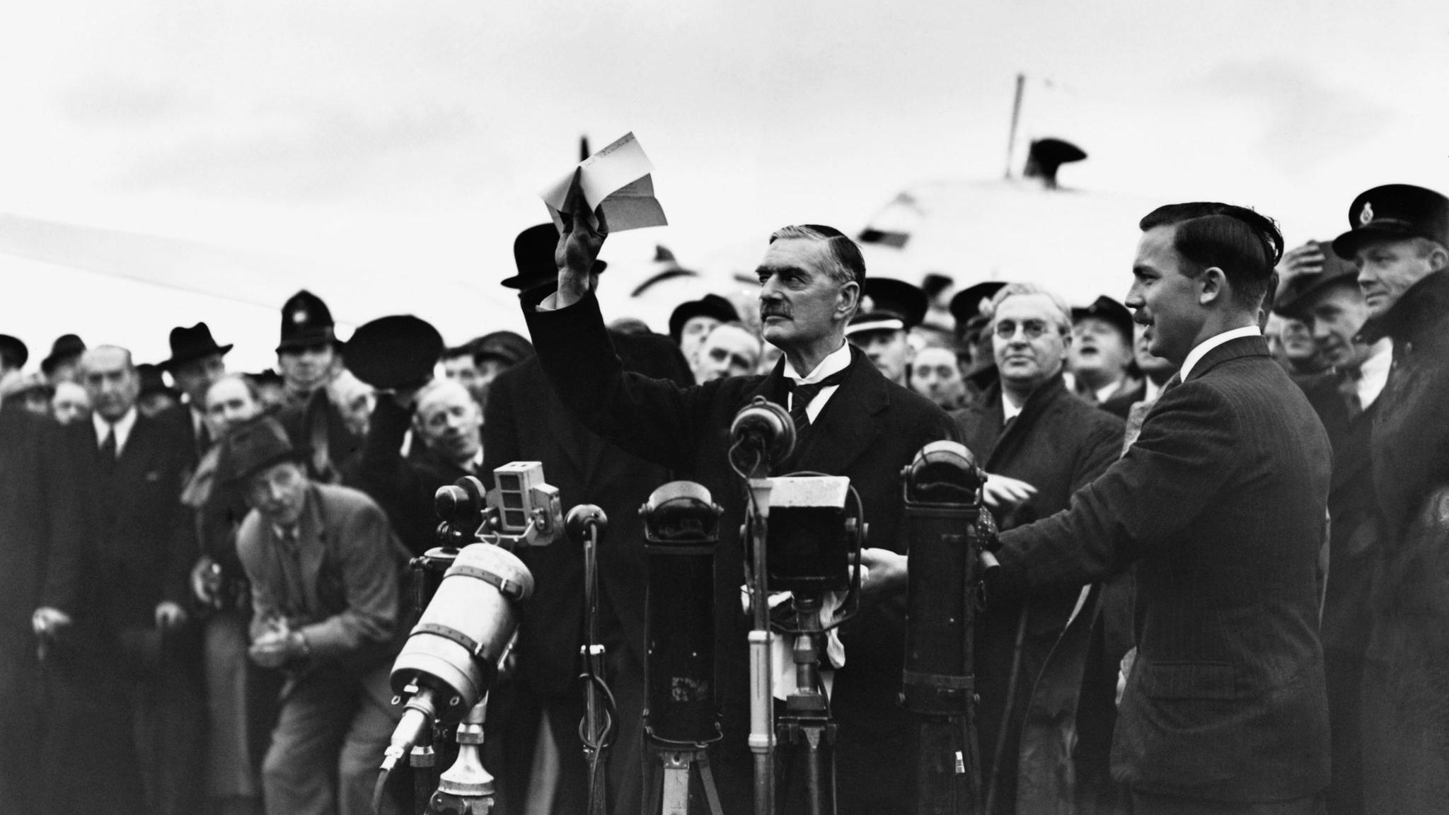 Der britische Premier Neville Chamberlain steht vor mehreren Mikrofonen.