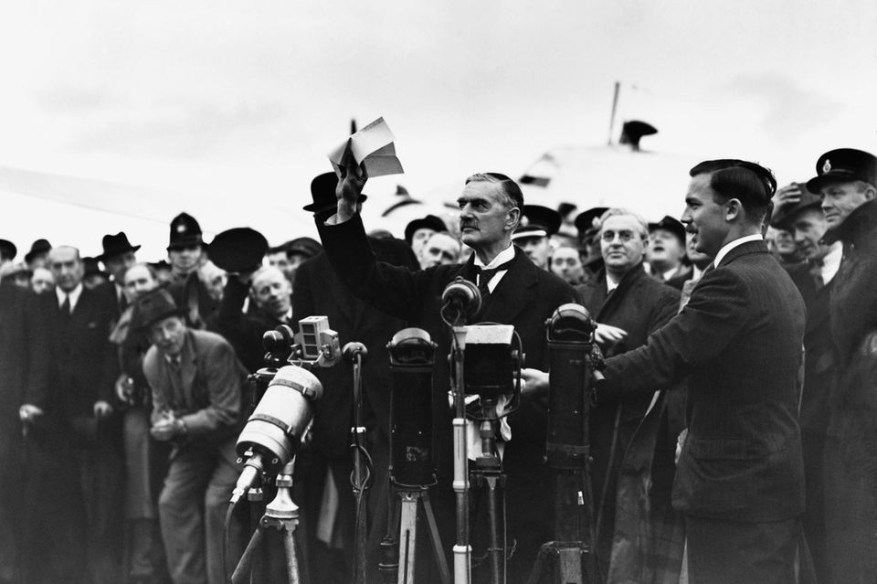 Der britische Premier Neville Chamberlain steht vor mehreren Mikrofonen.