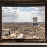 Durch ein Fenster sieht man auf die kasachische Steppenlandschaft mit weißen Gebäuden.