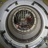 Kreisrunde Schleuse im Inneren einer Raumfähre, um die Luke sind Griffe für die schwebenden Kosmonauten.