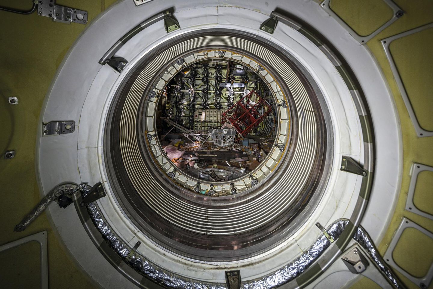 Kreisrunde Schleuse im Inneren einer Raumfähre, um die Luke sind Griffe für die schwebenden Kosmonauten.