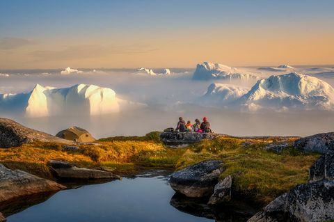 Vier Personen sitzen auf einem felsigen Untergrund und schauen auf den Eisfjord