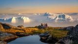 Vier Personen sitzen auf einem felsigen Untergrund und schauen auf den Eisfjord