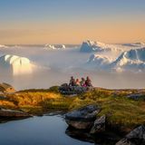 Vier Personen sitzen auf einem felsigen Untergrund und schauen auf den Eisfjord