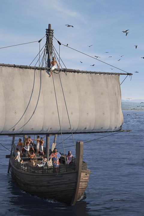 Ein offenes Holzschiff mit breitem Segel und elf Männern an Bord auf dem Meer, vor einem Küstenstreifen