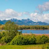 Man sieht die Berge mit Schneegipfeln, vorne den See mit Wald und Wiesen.