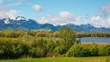 Man sieht die Berge mit Schneegipfeln, vorne den See mit Wald und Wiesen.