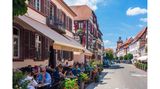 Menschen sitzen im Außenbereich eines Restaurants und genießen ihr Essen bei Sonnenschein