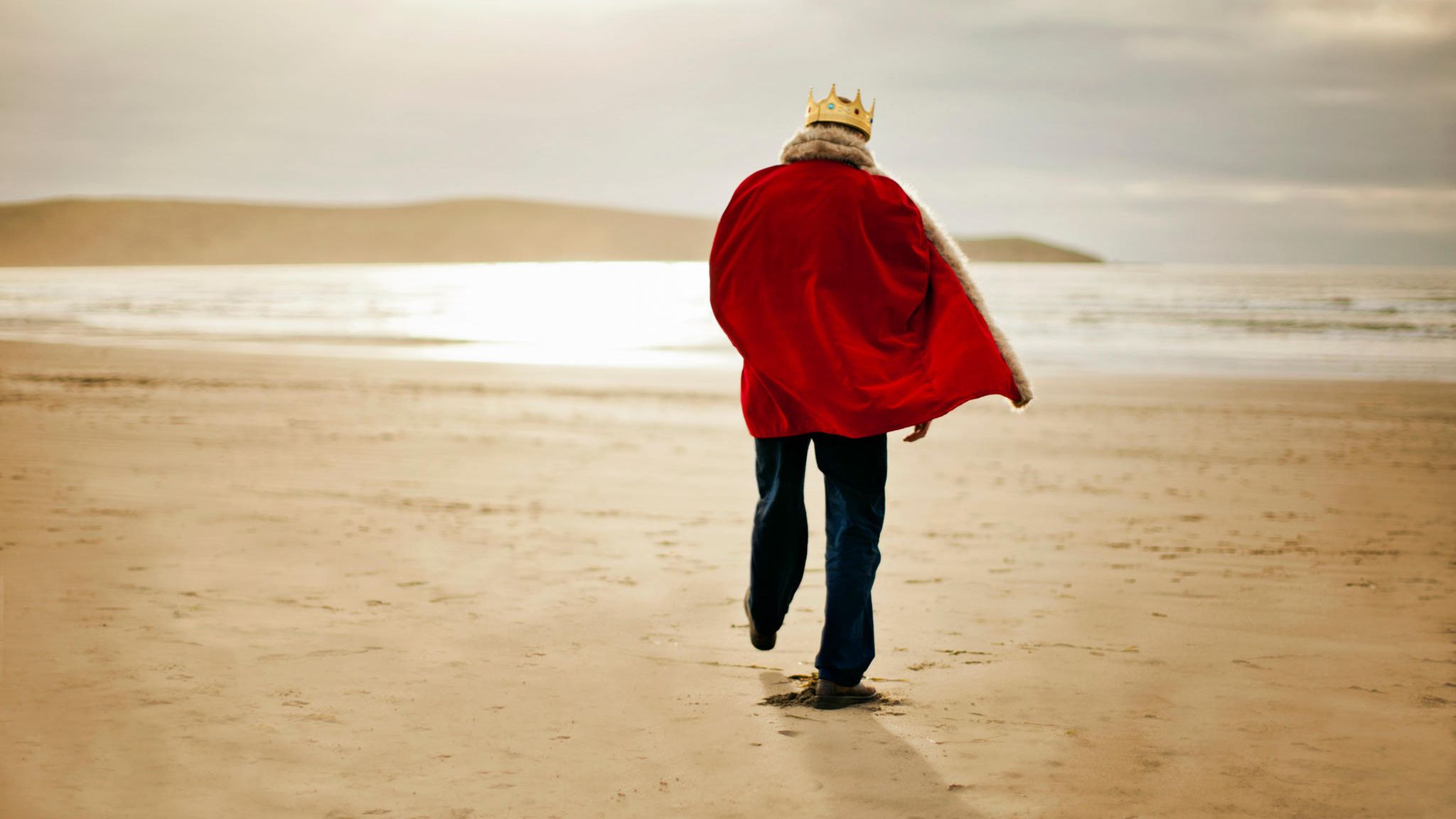 Ein Mann der gekleidet ist wie ein König spaziert am Strand