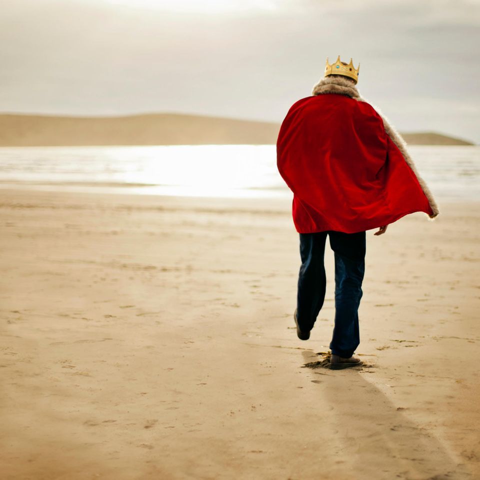 Ein Mann der gekleidet ist wie ein König spaziert am Strand
