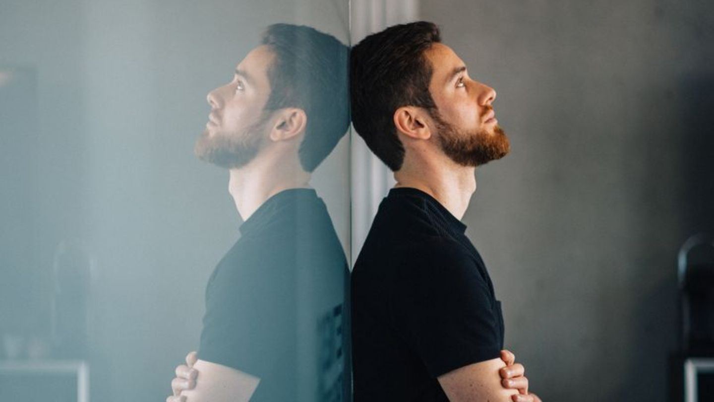 Ein schwarz angezogener Mann lehnt an einer spiegelnden Wand in Gedanken versunken