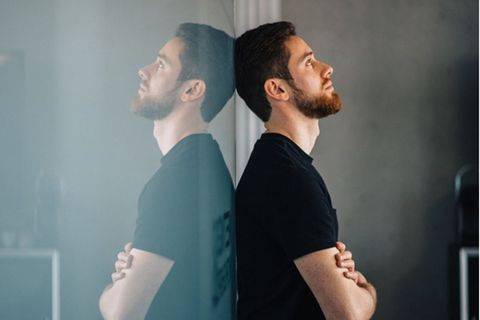 Ein schwarz angezogener Mann lehnt an einer spiegelnden Wand in Gedanken versunken