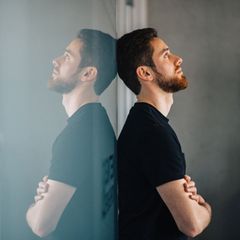 Ein schwarz angezogener Mann lehnt an einer spiegelnden Wand in Gedanken versunken