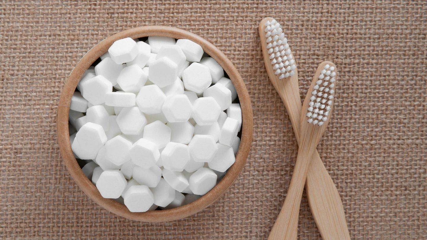 Eine Schale ist mit sechseckigen Zahnputztabletten gefüllt, daneben liegen zwei Bambus-Zahnbürsten über kreuz