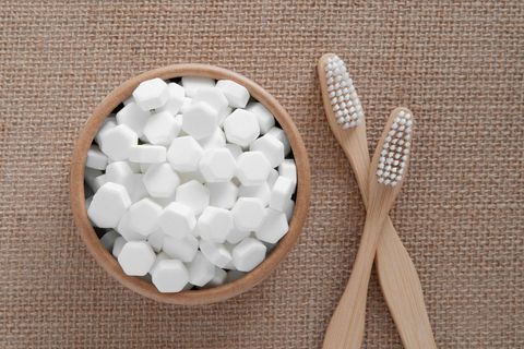 Eine Schale ist mit sechseckigen Zahnputztabletten gefüllt, daneben liegen zwei Bambus-Zahnbürsten über kreuz