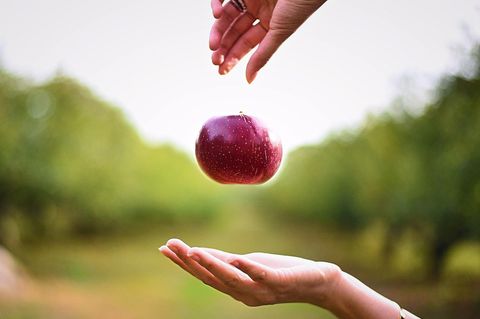 Eine Frau lässt einen Apfel von einer Hand in die andere fallen