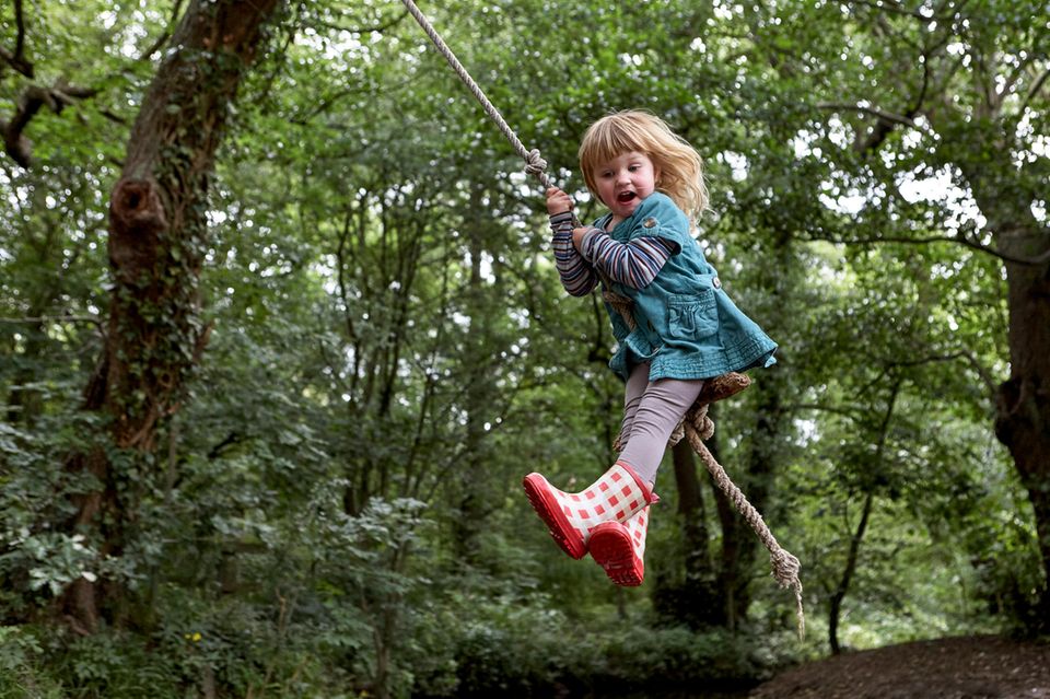 Ein Mädchen schaukelt an einem Tau im Wald.  1.3644