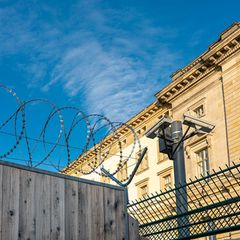 Gefängnismauer mit Stacheldraht unter blauem Himmel