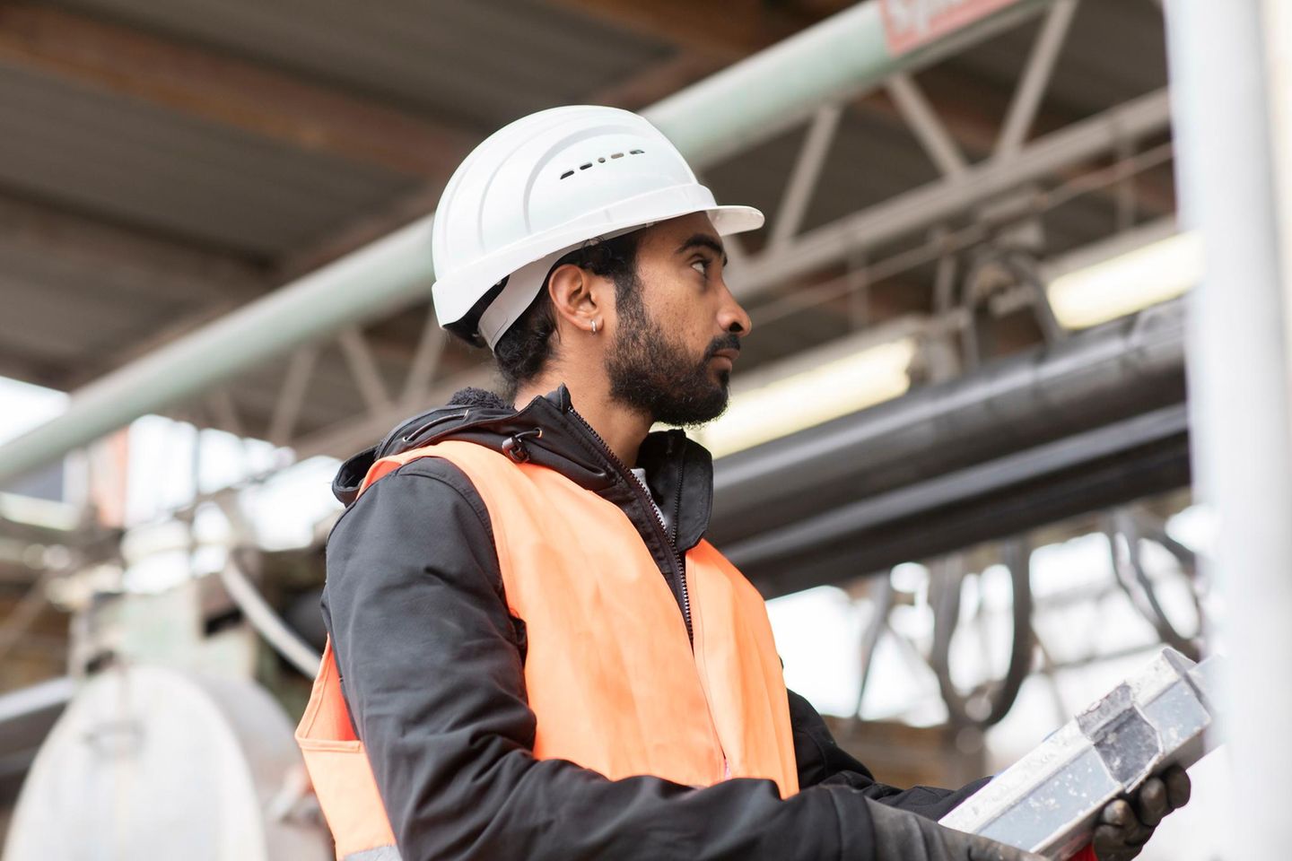 Mann mit Migrationshintergrund bei der Arbeit mit Helm auf dem Kopf auf einer Baustelle