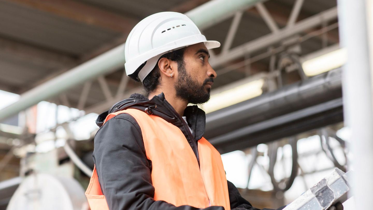 Mann mit Migrationshintergrund bei der Arbeit mit Helm auf dem Kopf auf einer Baustelle