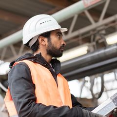 Mann mit Migrationshintergrund bei der Arbeit mit Helm auf dem Kopf auf einer Baustelle