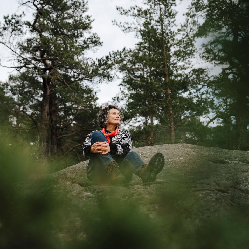 Eine Frau sitzt auf einem Felsen im Wald