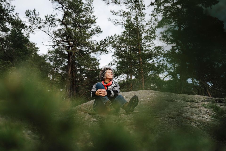 Eine Frau sitzt auf einem Felsen im Wald