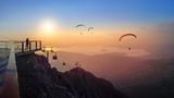 Blick von einem Berg aus auf Paraglider in Abendstimmung
