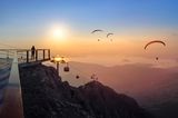 Blick von einem Berg aus auf Paraglider in Abendstimmung