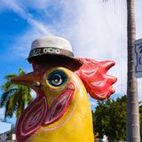 Eine Huhnfigur steht vor dem Straßenschild der Calle Ocho in Miami. Das Huhn hat einen Gut auf und eine Zigarre im Schnabel