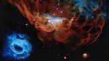 Aus Gasen. Die Nebel in der Großen Magellanschen Wolke, einer Nachbargalaxie der Milchstraße, erinnern an Korallen. Deswegen trägt die Aufnahme des Weltraumteleskops "Hubble" den Spitznamen "Cosmic Reef". Der rötliche Nebel NGC 2014 ist eine Geburtsstätte neuer Sterne. Die Exemplare, die in seinem Zentrum funkeln, sind zehn- bis zwanzigmal massereicher als die Sonne. Mit ihrer ultravioletten Strahlung erhitzen sie das umgebende Gas. Doch sie sind mickrig verglichen mit dem Giganten, der den blauen Nebel unten links schuf. Er leuchtet 200.000-mal heller als die Sonne. Bei Eruptionen stieß er Material aus seiner äußeren Hülle ab. Das fortgeschleuderte Gas umgibt ihn nun wie ein kosmischer Rauchring.  KW 42