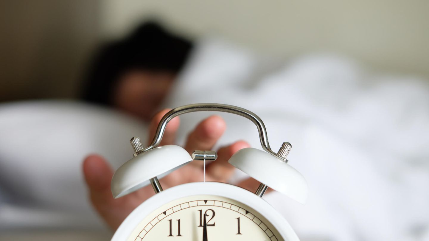 Eine Frau im Bett drück auf die Snooze-Taste ihres Weckers Eine Frau im Bett drück auf die Snooze-Taste ihres Weckers