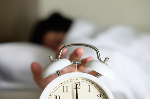 Eine Frau im Bett drück auf die Snooze-Taste ihres Weckers
