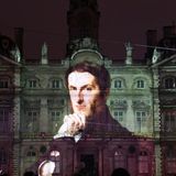 Ein Mann mit Hand am Kinn wird auf eine Schlossfassade projeziert.