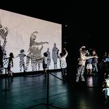 Tanzende Menschen in einem Raum, projiziert auf eine beleuchtete Leinwand