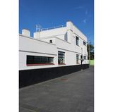 Haus mit Flachdach und Balkonbrüstung, breite Sprossenfenster, schönes Wetter.