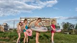 Vier Kinder in Schwimmkleidung auf einer Wiese vor einem Haus