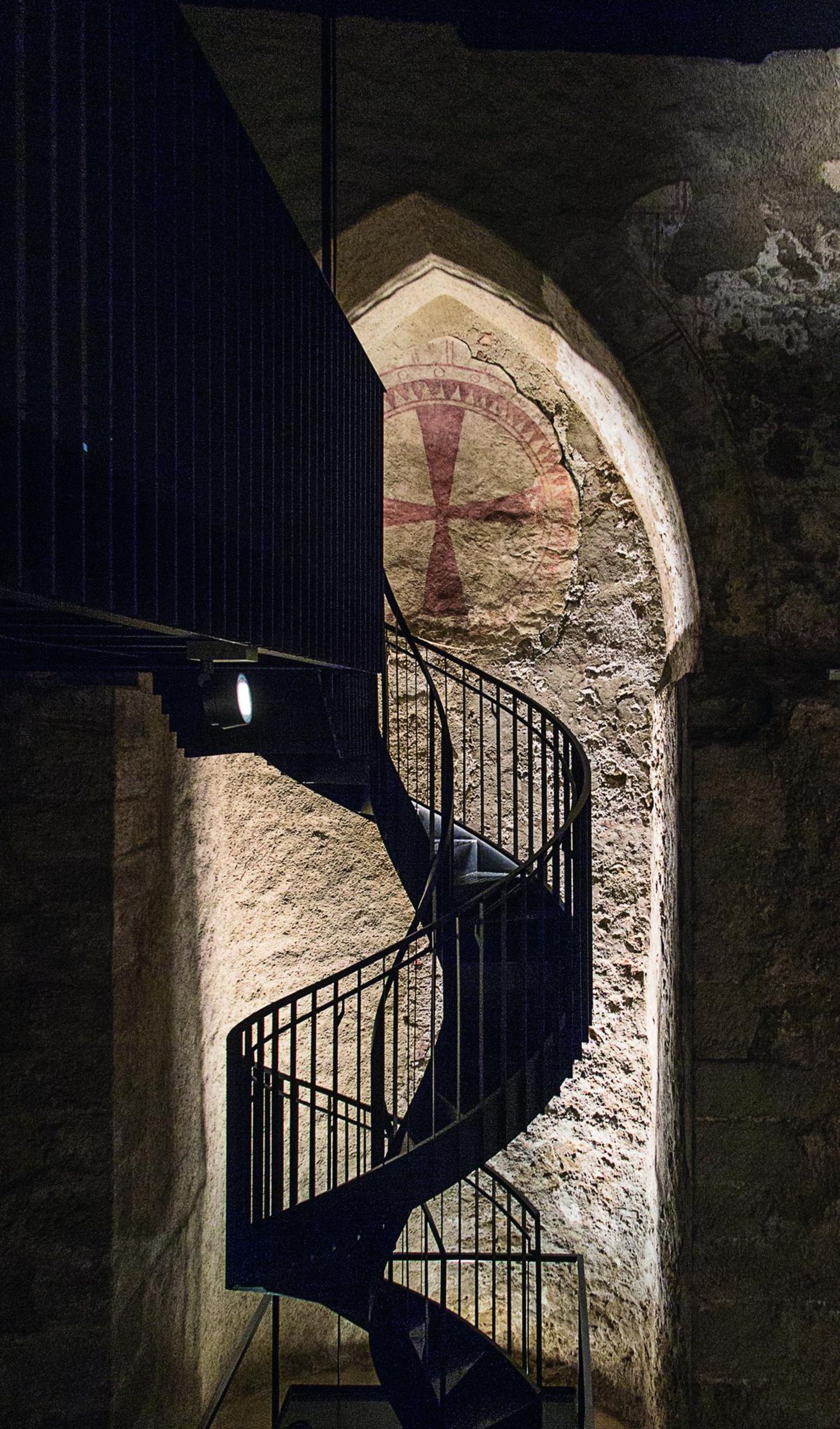 Unterirdisch: die Virgilkapelle Wendeltreppe im Dunkeln, angeleuchtet das byzantinische Kreuz an der Wand.