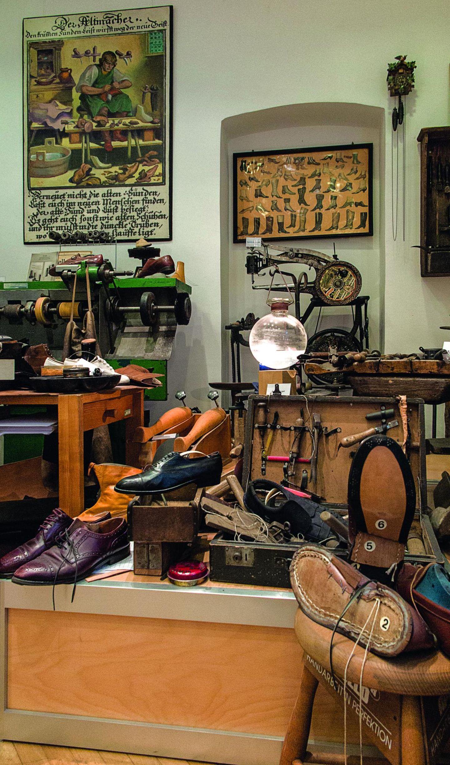 Kaiser- und Clownsgaloschen: das Schuhmuseum Nähmaschine, Bilder von Schuhen, auf dem Tisch alte Schuhe.
