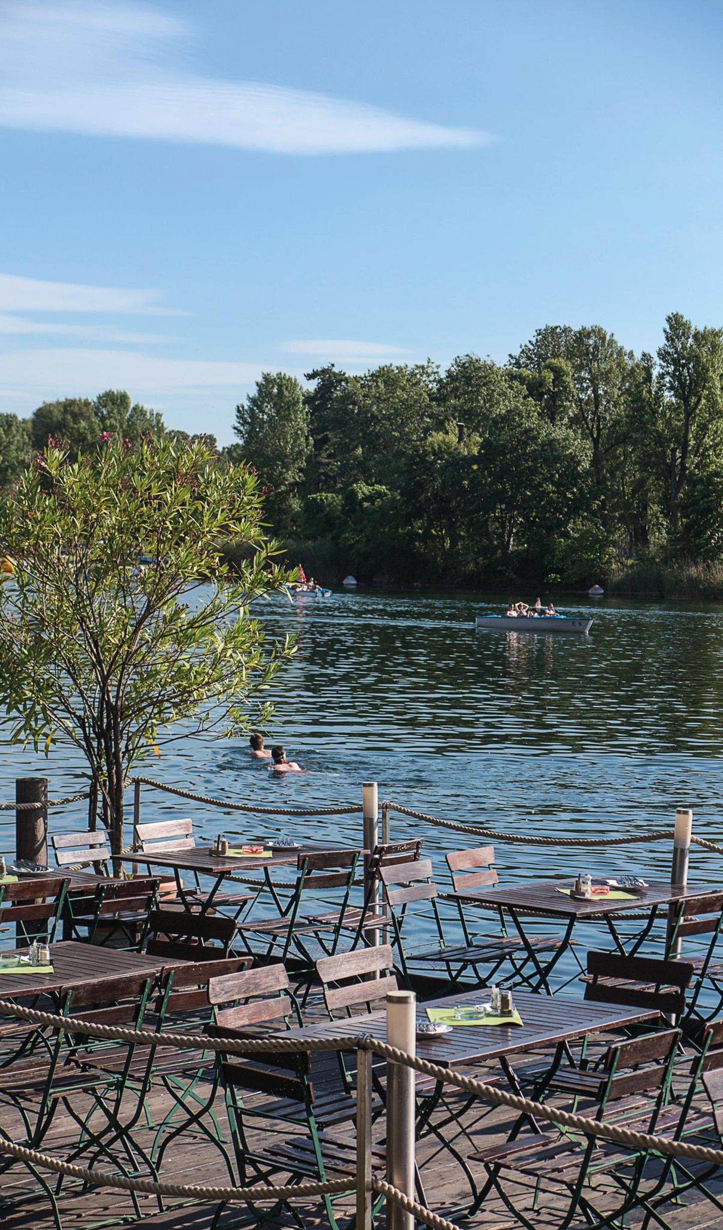 Neu Brasilien: das Bootshaus an der Alten Donau Tische und Stühle am Wasser der Alten Donau, darin Schwimmer.