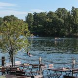 Tische und Stühle am Wasser der Alten Donau, darin Schwimmer.